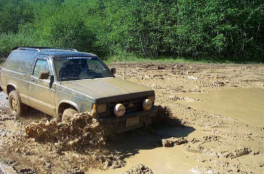 Muddy tan two-door Chevy SUV splashing through a mud pit off-road
