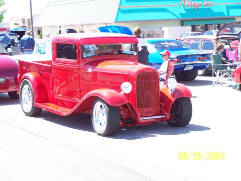 1972 Ford Ranchero - A vintage red pickup truck is displayed at a car show with other vehicles and spectators.