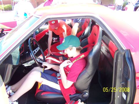 1972 Ford Ranchero - A boy sits in the driver's seat of a red car with racing seats, with another person visible in the background.