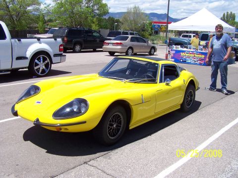 1972 Ford Ranchero - A bright yellow sports car is parked at an outdoor car show with other vehicles and a vendor tent in the background.