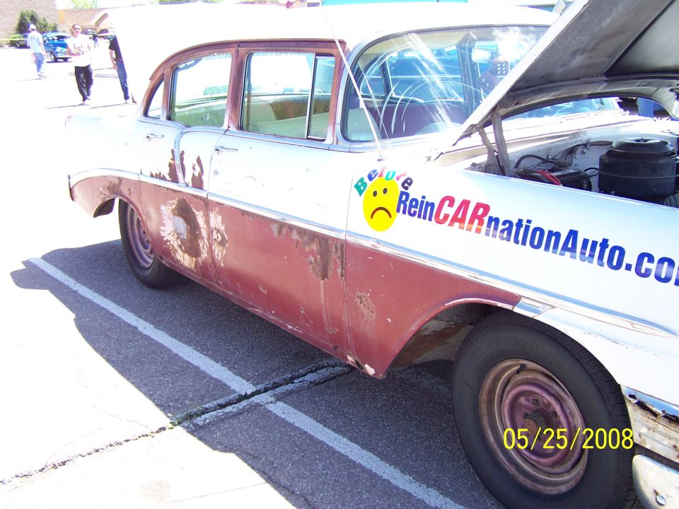 Side view of a rusty two-tone sedan with a "Be Sure ReinCARnationAuto.com" decal