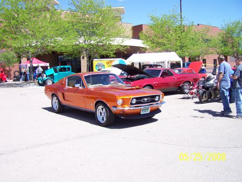1972 Ford Ranchero - An orange 1967 Ford Mustang is displayed at a car show alongside other vehicles and a motorcycle.