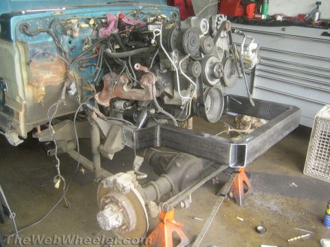 1987 Suzuki Samurai - The engine bay and chassis of a vehicle are visible, with the engine removed and the vehicle supported by jack stands.