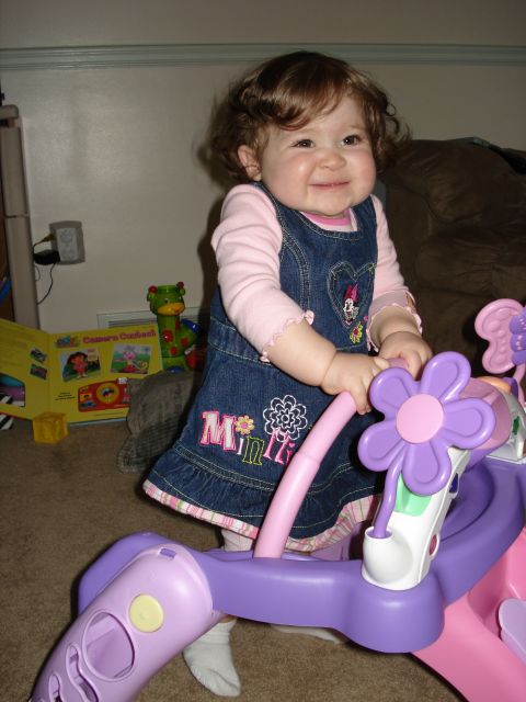 2000 Ford Crown Victoria - A smiling baby girl stands with a toy in a room with toys and a book.