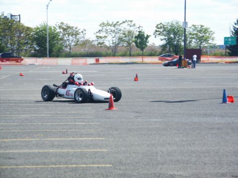 2001 Mercury Grand Marquis - A single-seater race car is driven on a paved lot marked with cones, suggesting a timed event or autocross event.