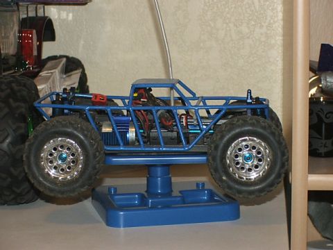 2000 Nissan Frontier - A blue remote control monster truck is displayed on a stand, with another vehicle partially visible to the left.