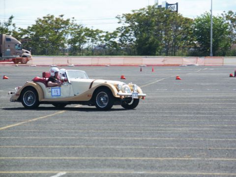 2001 Mercury Grand Marquis - A cream-colored convertible sports car, identified by racing number 18, navigates an asphalt course with orange cones.