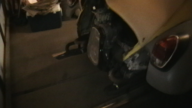 Rear of yellow VW Beetle in garage with engine exposed, taillight and fender visible