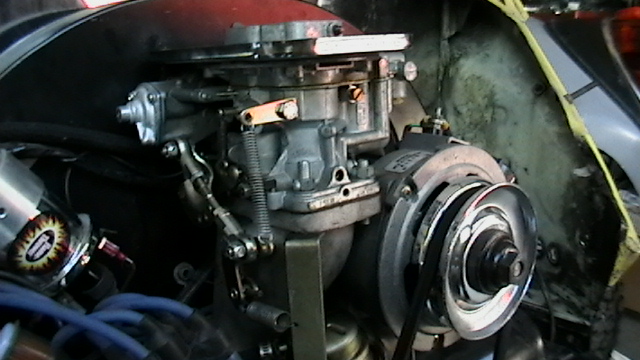 Close-up of Volkswagen Beetle engine showing carburetor, fan belt pulley, and blue spark plug wires
