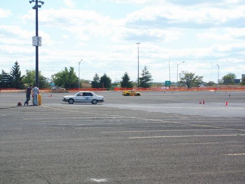 2001 Mercury Grand Marquis - A white sedan with racing numbers participates in an autocross event, with a yellow car visible in the background.