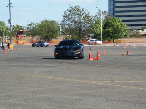 2001 Mercury Grand Marquis - A black sports car drives through an autocross course with orange cones marking the path. Other vehicles are visible in the distance.