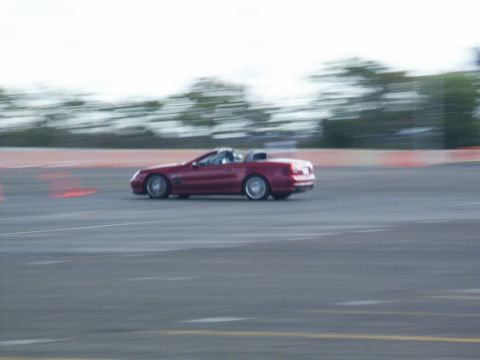 2001 Mercury Grand Marquis - A red convertible sports car is captured in motion on a track, with motion blur indicating speed.