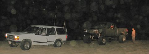 1984 Ford Bronco - Two modified vehicles are parked on a sandy area at night, with a person standing near the truck.