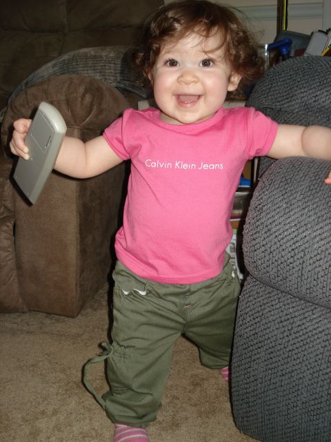 2000 Ford Crown Victoria - A baby stands between two couches, holding a remote control and wearing a pink t-shirt with 'Calvin Klein Jeans' on it.