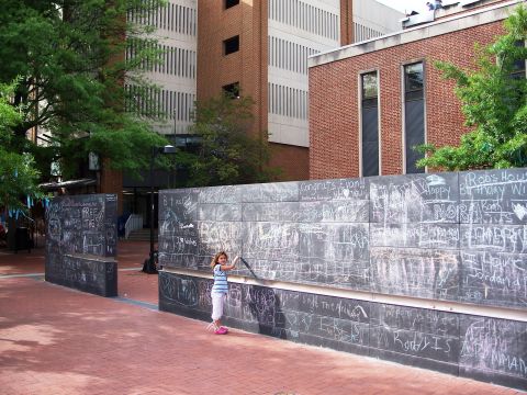 1971 Ford Ranchero - A child in a striped tank top writes on a long public chalkboard wall covered in colorful messages such as "Congrats Evan!!" and "Happy Bir…