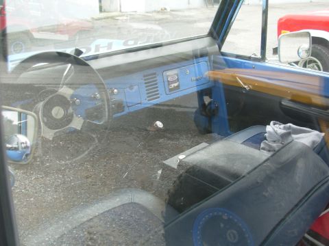 1975 Ford Bronco - The interior of a blue Ford Bronco is seen, with a red truck visible through the window.