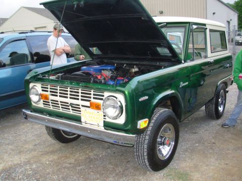 1975 Ford Bronco - A green 1975 Ford Bronco is displayed with its hood open, revealing the engine compartment.