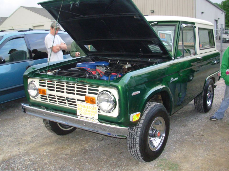 Dark green early Ford Bronco with hood up showing V8, front 3/4 at a show