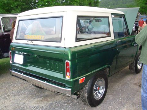 1975 Ford Bronco - This green 1975 Ford Bronco features a white hardtop and is seen from the rear three-quarter angle.