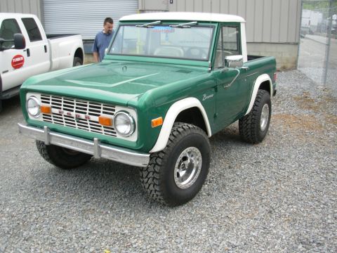 1975 Ford Bronco - A green 1975 Ford Bronco with a white top is parked next to a white pickup truck.
