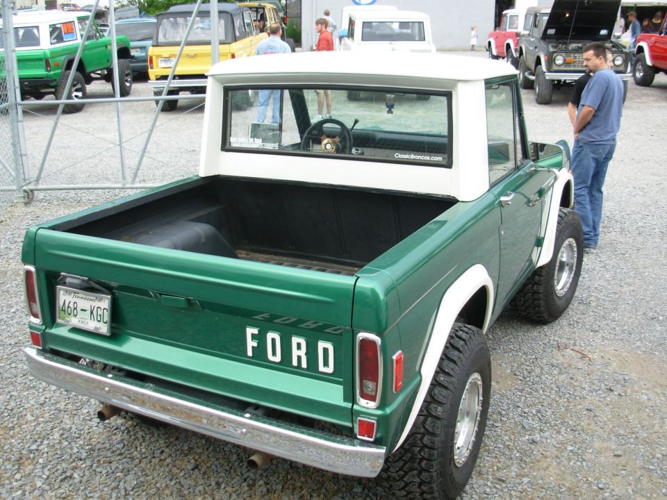 Green early Bronco half-cab pickup with white roof, rear 3/4 view at a Bronco show