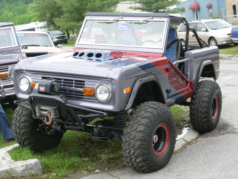 1975 Ford Bronco - This heavily modified Ford Bronco features oversized tires and a prominent hood scoop, parked next to another Bronco.