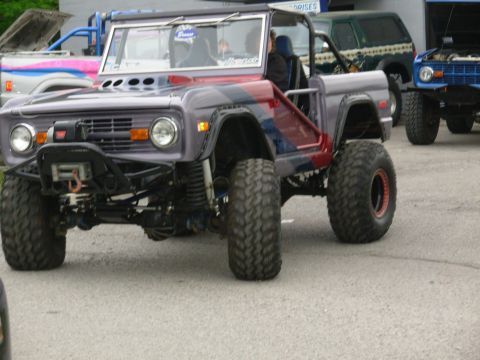 1975 Ford Bronco - A modified 1975 Ford Bronco with custom paint and off-road tires is parked with other vehicles.