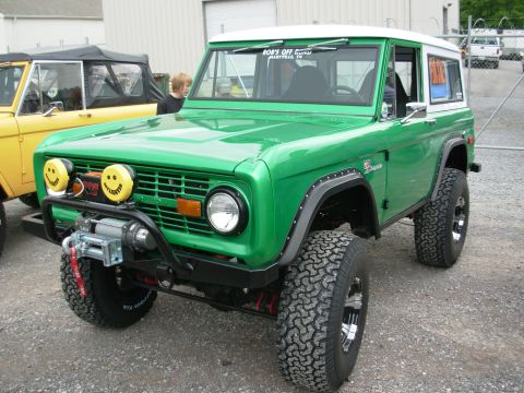 1975 Ford Bronco - Green 1975 Ford Bronco parked next to a yellow Bronco, custom smiley face fog lights.