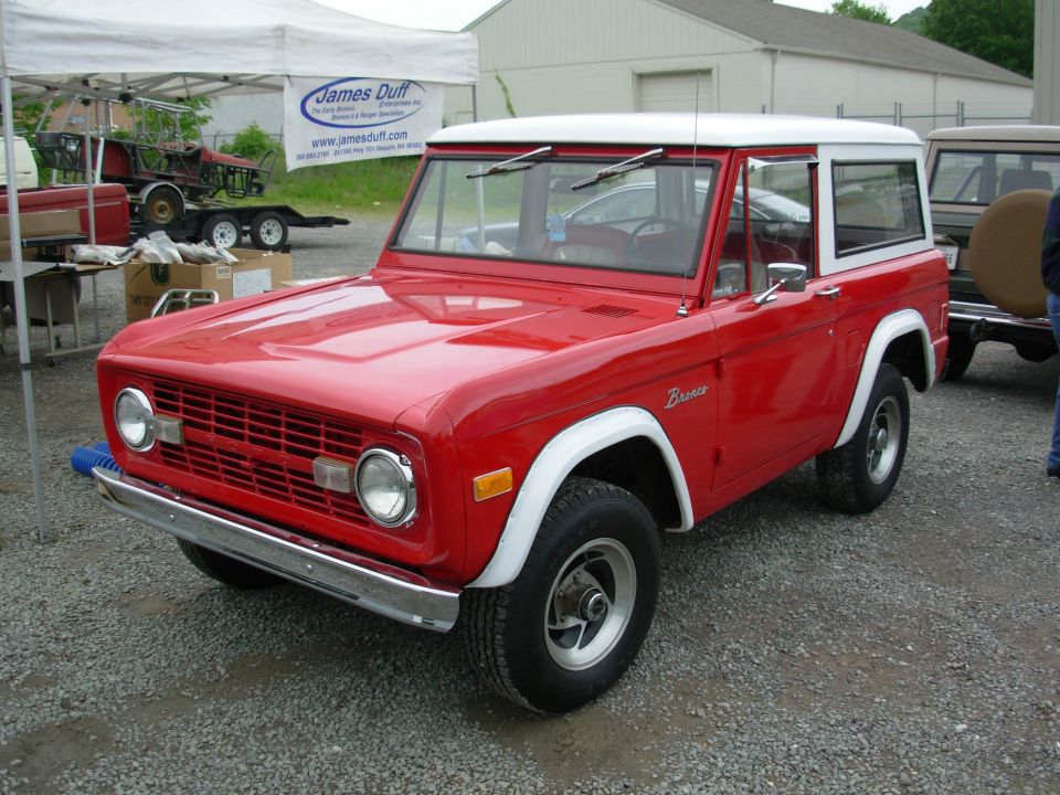 Red early Ford Bronco with white hardtop, front 3/4 view at a Bronco show