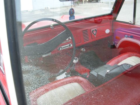 1975 Ford Bronco - The interior of a classic red SUV is visible, with gravel on the floor and a heart emblem on the dash.