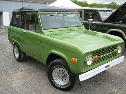 1975 Ford Bronco - A green 1975 Ford Bronco is parked next to another Bronco with its hood open.