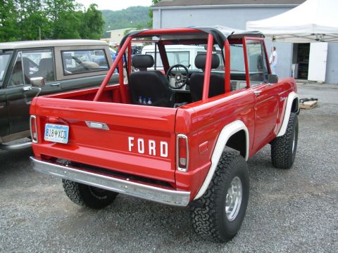 1975 Ford Bronco - A red 1975 Ford Bronco is parked next to another vehicle, with a white tent in the background.