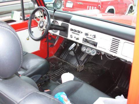 1975 Ford Bronco - Interior view of a 1975 Ford Bronco, black seats, an aftermarket steering wheel, and auxiliary gauges on the dashboard.