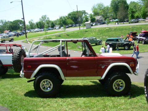 1975 Ford Bronco - A red 1975 Ford Bronco with a roll cage is parked on the grass at an outdoor event.