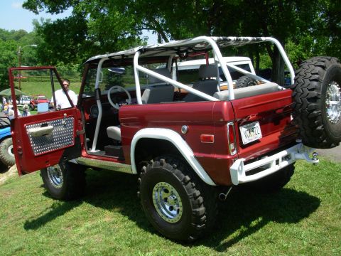 1975 Ford Bronco - A red Ford Bronco is parked on grass with its door open. Another vehicle is visible in the background.