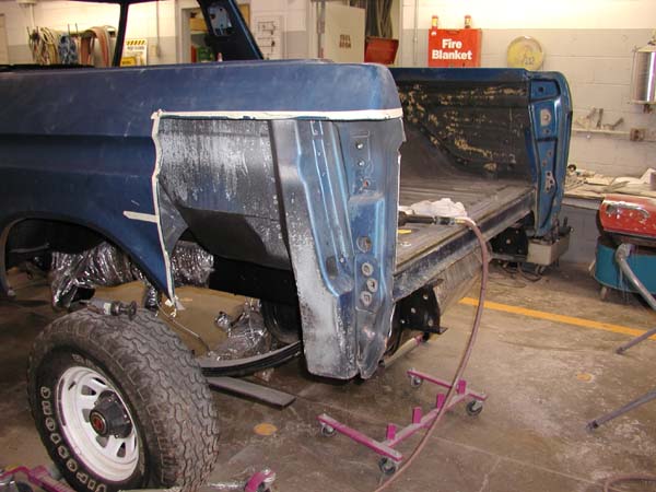 Blue truck body and bed pulled apart inside a shop during restoration, fire blanket on wall