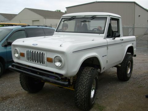 1975 Ford Bronco - A white Ford Bronco is parked outside next to a blue minivan, with a building in the background.