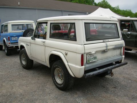 1975 Ford Bronco - A white 1975 Ford Bronco is parked behind a blue Bronco, with other vehicles visible in the background.