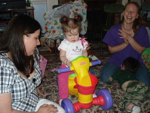 2000 Ford Crown Victoria - A baby sits on a tricycle while two women and a young boy are present in a room.