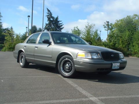2000 Ford Crown Victoria - A gray 2000 Ford Crown Victoria is shown from the front three-quarter view in a parking lot under a partly cloudy sky.