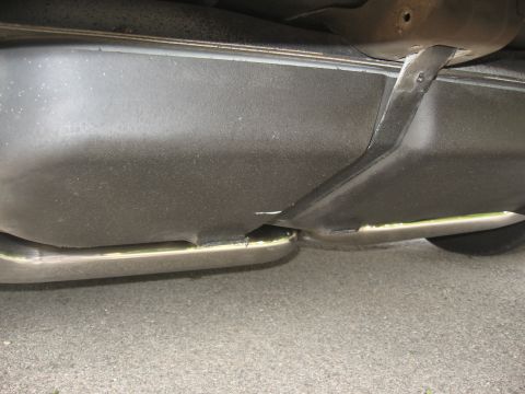 1998 Ford Taurus - The underside of a vehicle shows a black plastic undertray with a silver exhaust pipe visible beneath it. A metal bracket is attached to th…