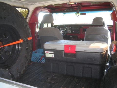 1979 Ford Bronco - The interior of a 1979 Ford Bronco shows a large spare tire secured with an orange strap on the left, and a black storage container with a…