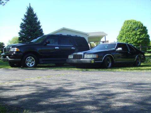 1996 Ford Bronco - Two black vehicles are parked on a paved surface in front of a house. The vehicle on the left is a large SUV, and the vehicle on the right…