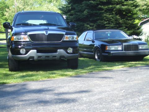 1996 Ford Bronco - A black Lincoln Navigator SUV is parked on the grass next to a black Lincoln Mark VIII coupe. The SUV is in the foreground and angled towar…