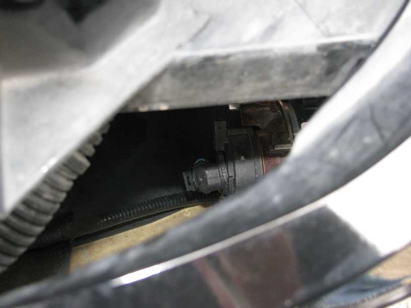 Close-up of a black electrical connector with a wire loom on a vehicle.
