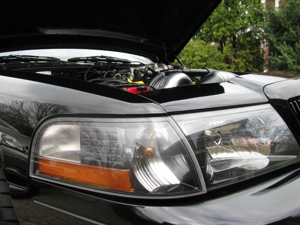 Close-up of black vehicle front headlight and amber turn signal with hood open showing engine