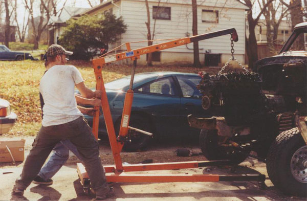engine hoist lifting an engine, with a car in the background