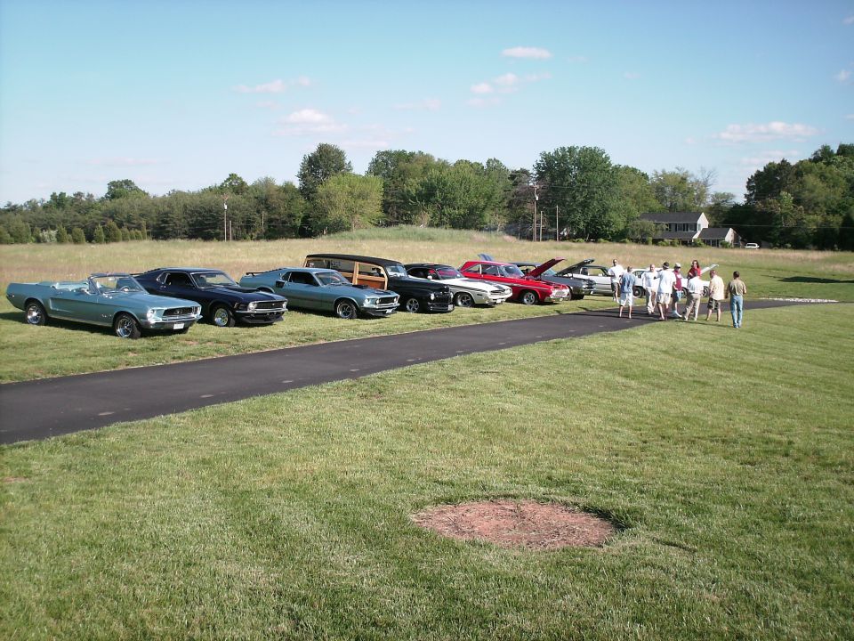 Several classic cars parked in a line on a paved surface with people gathered around.