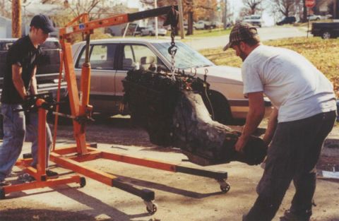 1978 Ford Bronco - Two men work to remove an engine from a vehicle using an engine hoist.