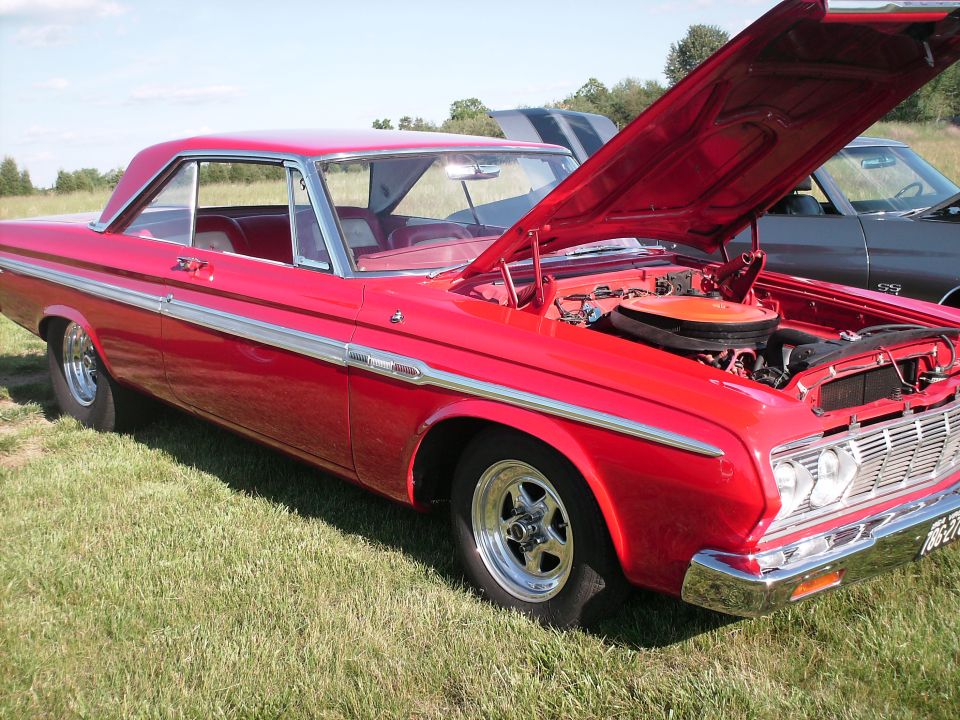 Red classic coupe with open hood showing engine, parked on grass.